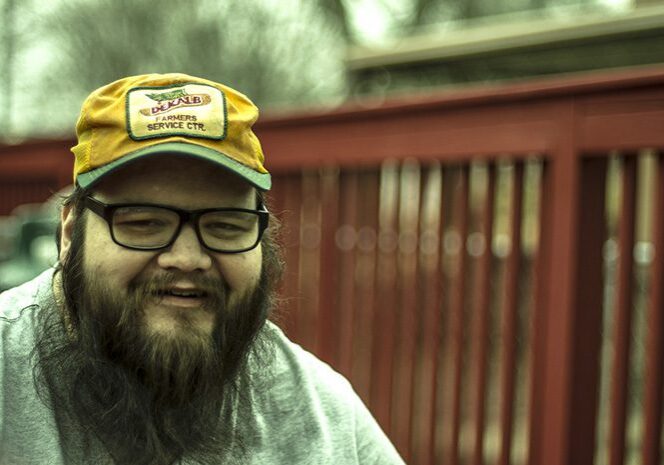 Man smiling, wearing yellow hat and glasses.