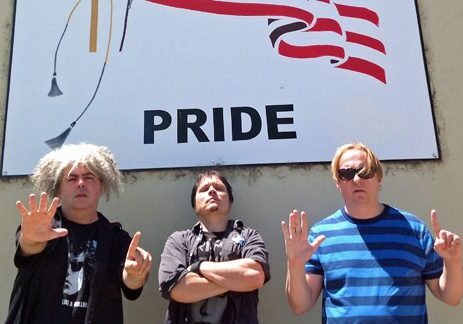 Three men posing under a pride sign.