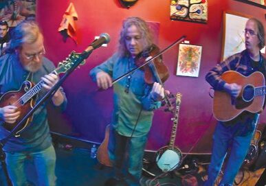 Three musicians performing with string instruments indoors.
