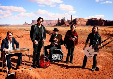 Band posing in desert with musical instruments.