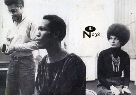 Three people sitting and standing indoors.