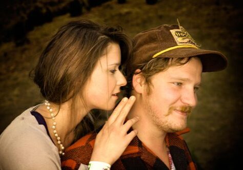 Woman whispering to man wearing a cap.