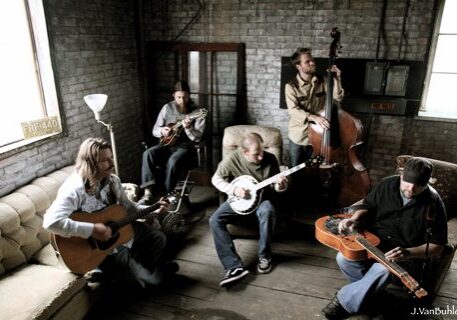 Band playing acoustic instruments in rustic room.