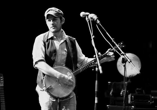 Musician playing banjo on stage, black and white.