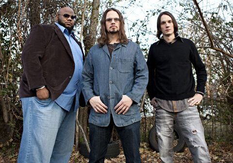 Three men standing in a wooded area.