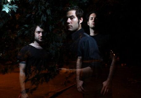 Three men standing in dark, leafy surroundings.