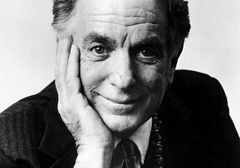 Elderly man smiling with hand on face.
