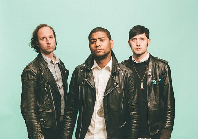 Three men wearing leather jackets, serious expressions.