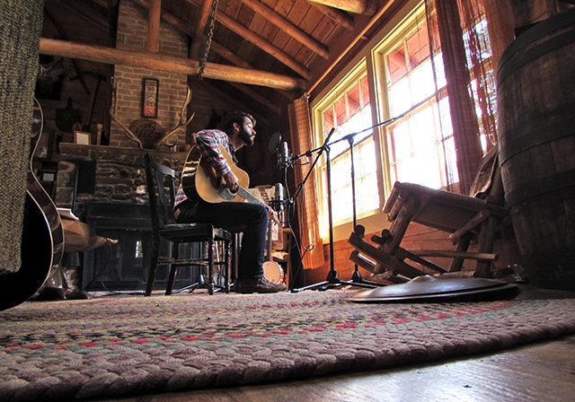 Musician playing guitar in rustic cabin.