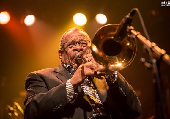Musician playing trombone under stage lights.