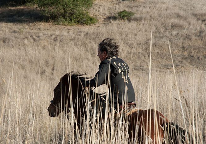 Person riding horse through dry grassland.