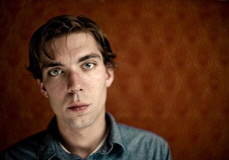 Man in denim shirt, orange background.