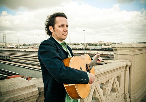 Man holding guitar on a bridge.