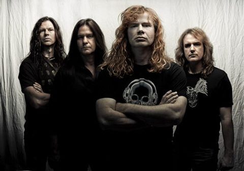 Rock band members standing against white backdrop.