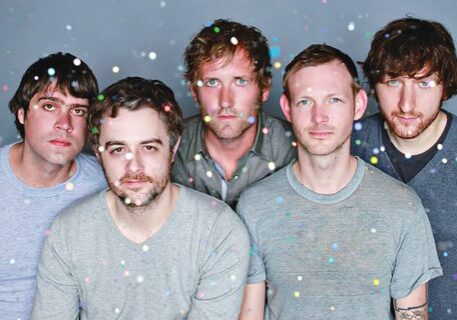 Five men with confetti, serious expressions.