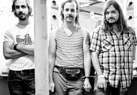 Three men standing in a dressing room.