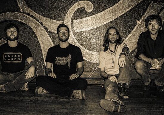 Four men sitting against a decorative wall.