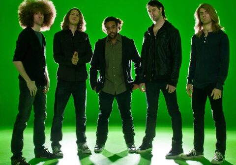Five people standing against a green background.