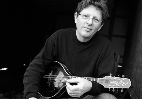 Man with mandolin sitting in dark room.