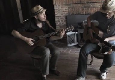 Two musicians playing acoustic guitars indoors.