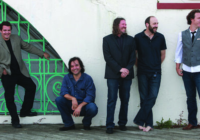 Five men standing and smiling against wall.