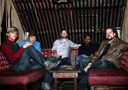 Five men sitting on a red couch.