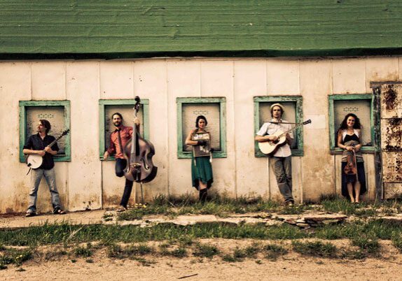 Five musicians standing with instruments in windows.