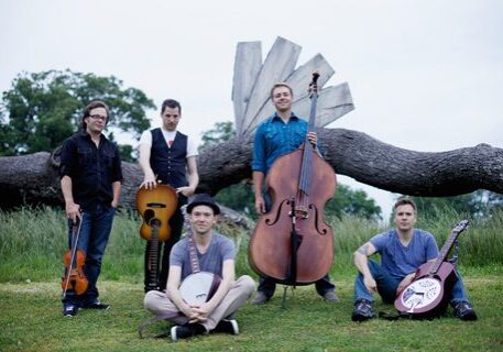 Band posing with instruments in outdoor setting.