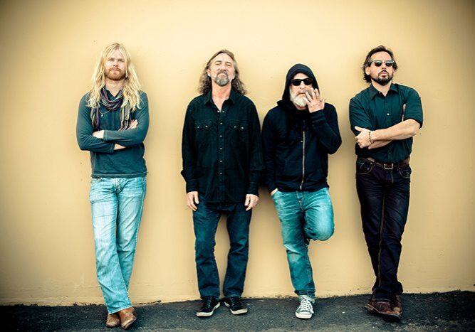 Four men standing against a yellow wall.