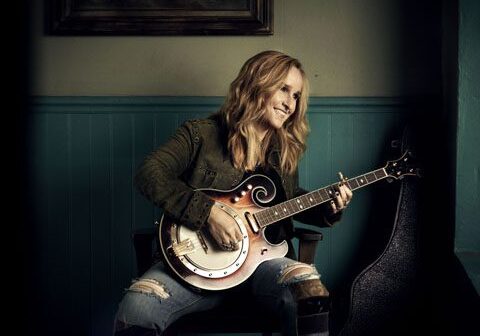 Person playing guitar while smiling indoors.