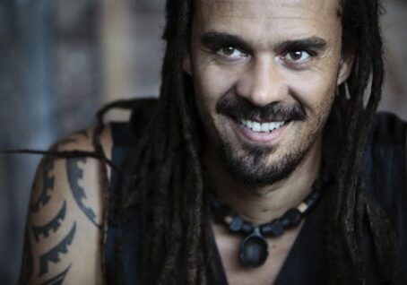 Smiling man with dreadlocks and tattoos.