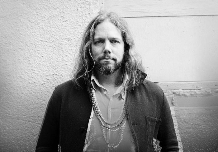 Man with long hair and beard, serious expression.