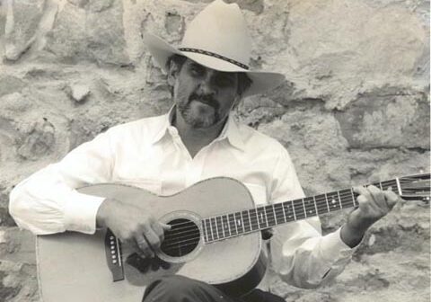Man in cowboy hat playing acoustic guitar.
