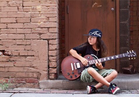Child playing guitar on urban street.