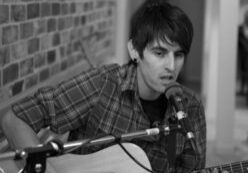 Singer playing guitar near brick wall.