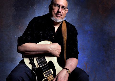 Man holding electric guitar against textured background.
