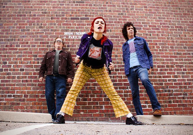 Three people posing against brick wall.