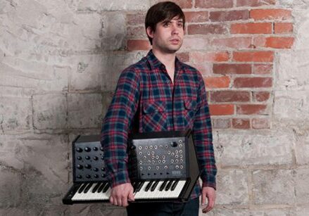 Man holding synthesizer against brick wall.