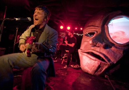 Musician performing on stage with large mask.
