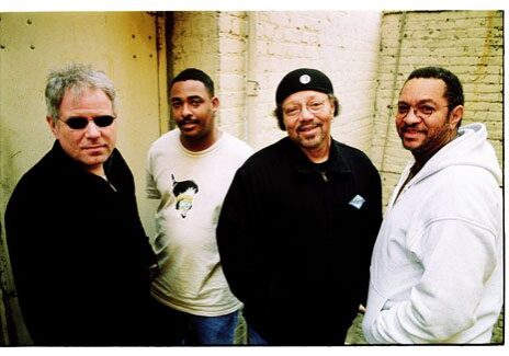 Four men standing against a brick wall.