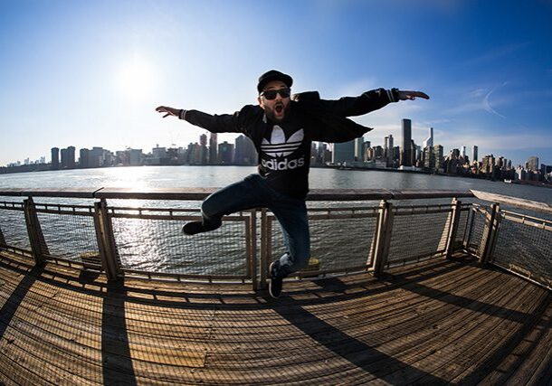 Man jumping on pier, cityscape in background.