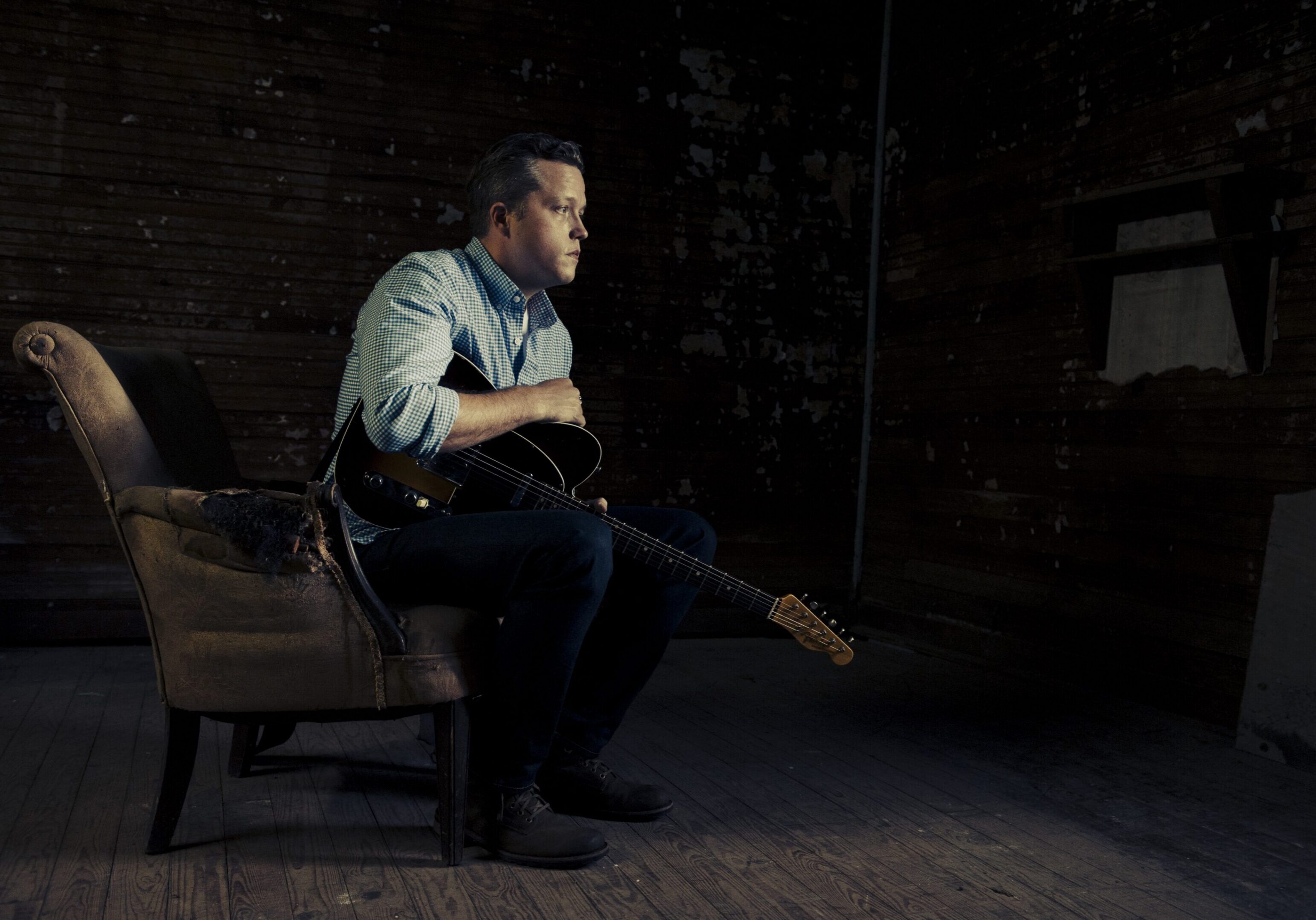 Man sitting with guitar in dimly lit room.