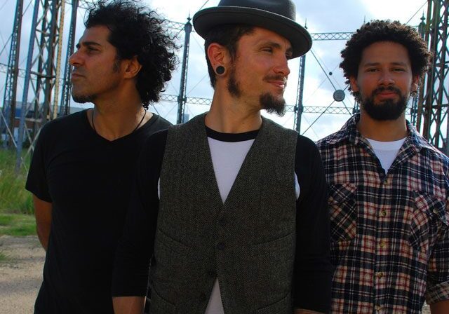 Three men standing outdoors near metal structures.