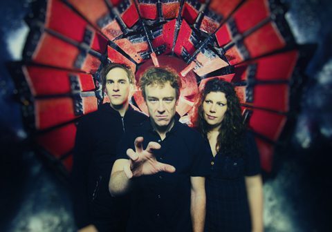 Three people posing in front of artwork.