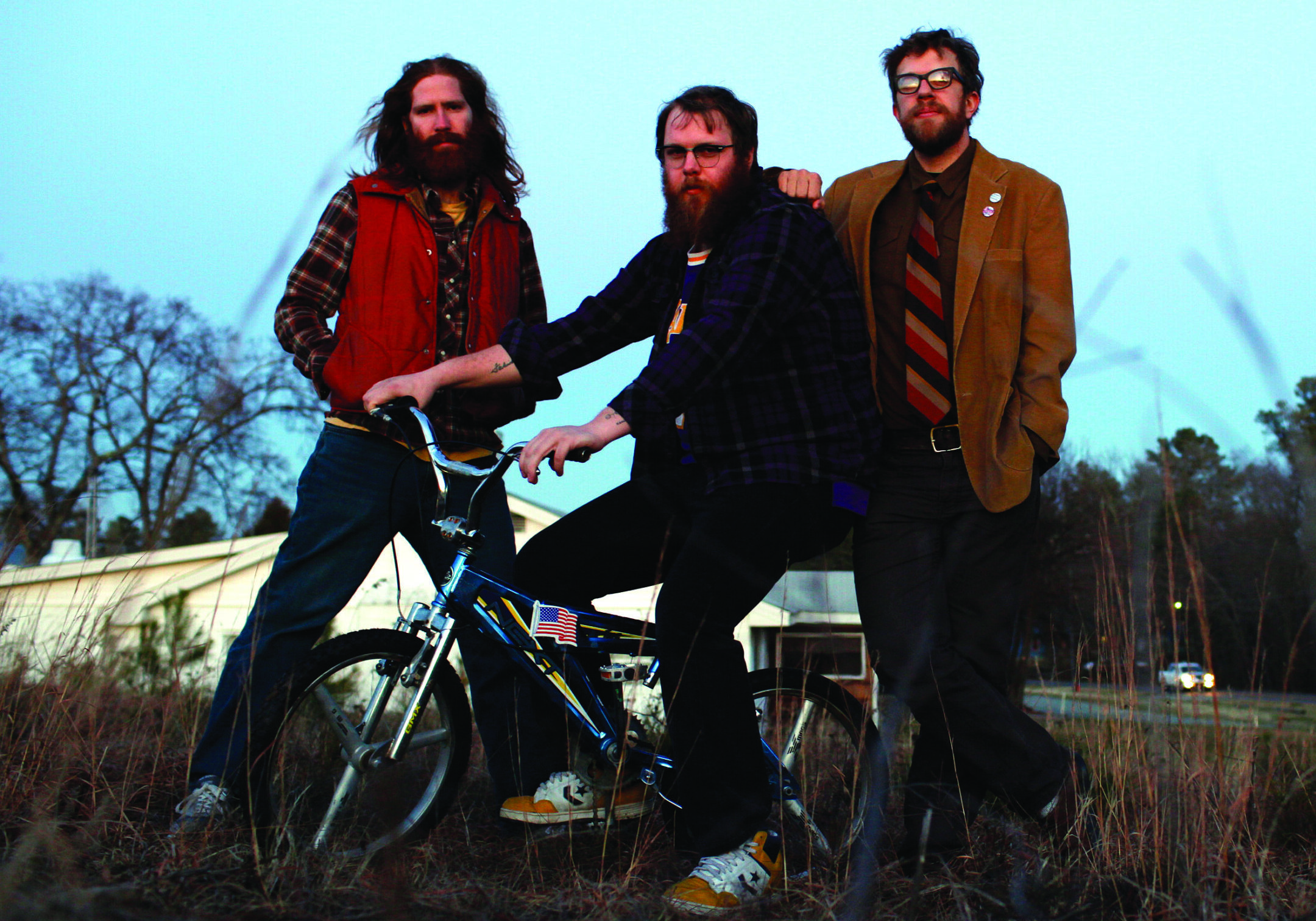 Three men with bicycle in rural setting.
