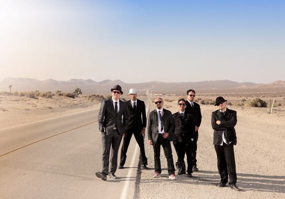 Band posing on desert road in suits.