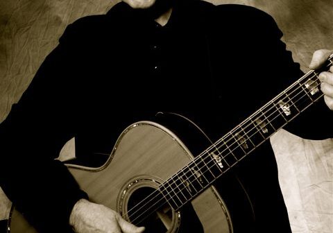 Man playing acoustic guitar, sepia-toned portrait.