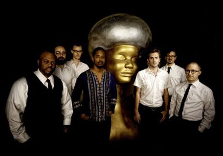 Seven men posing with large golden sculpture.