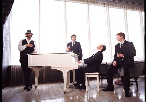 Four men gathered around a white piano.