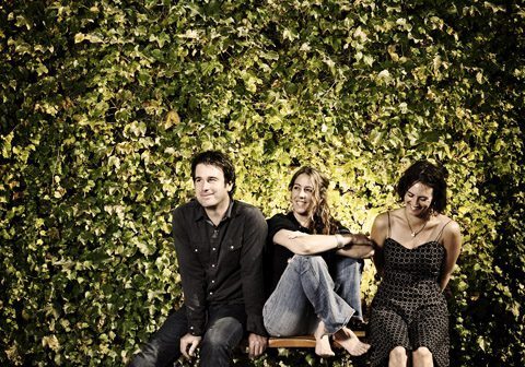 Three people sitting against a leafy wall.